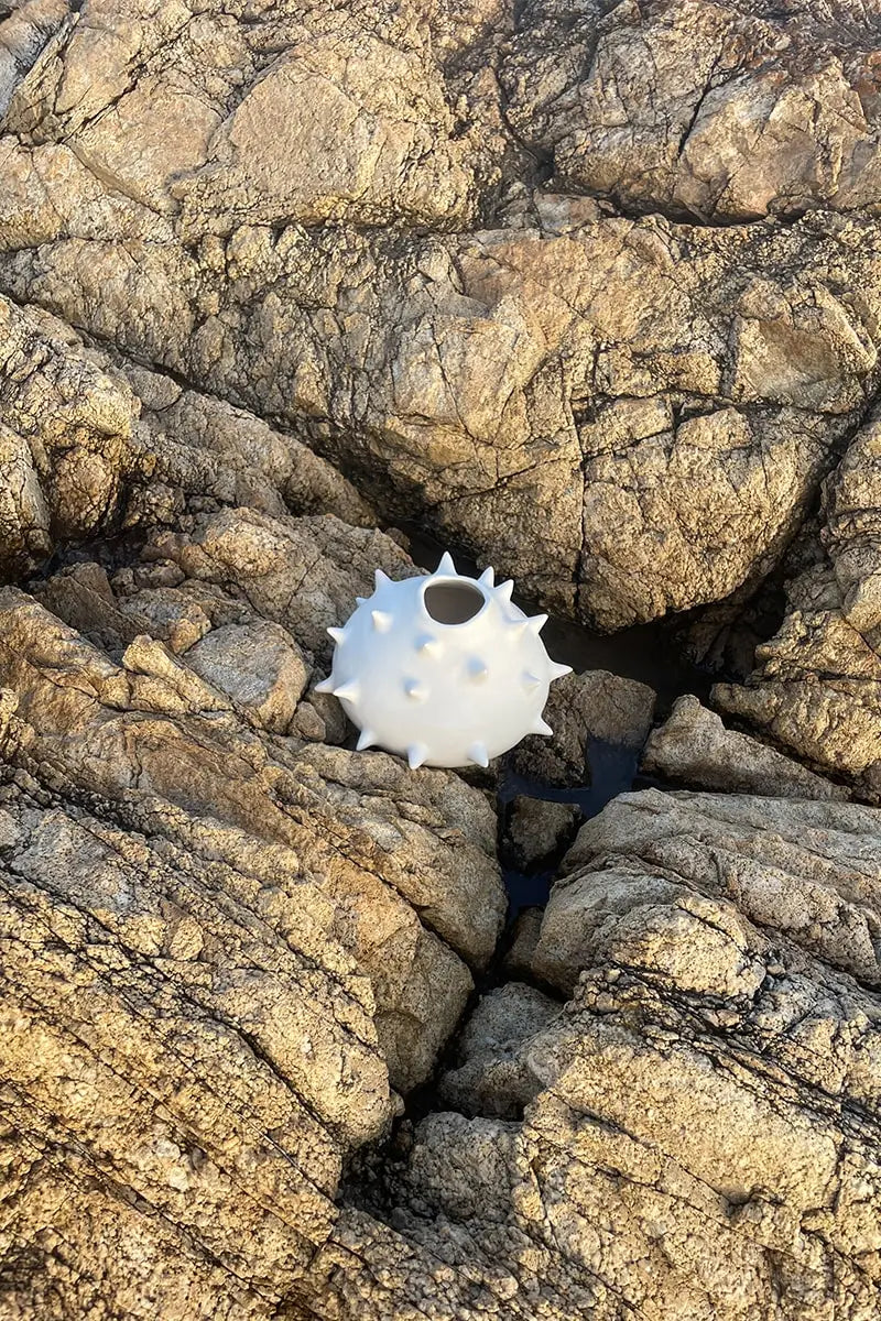 Handmade white round ceramic vase with spikes lying against the rocks